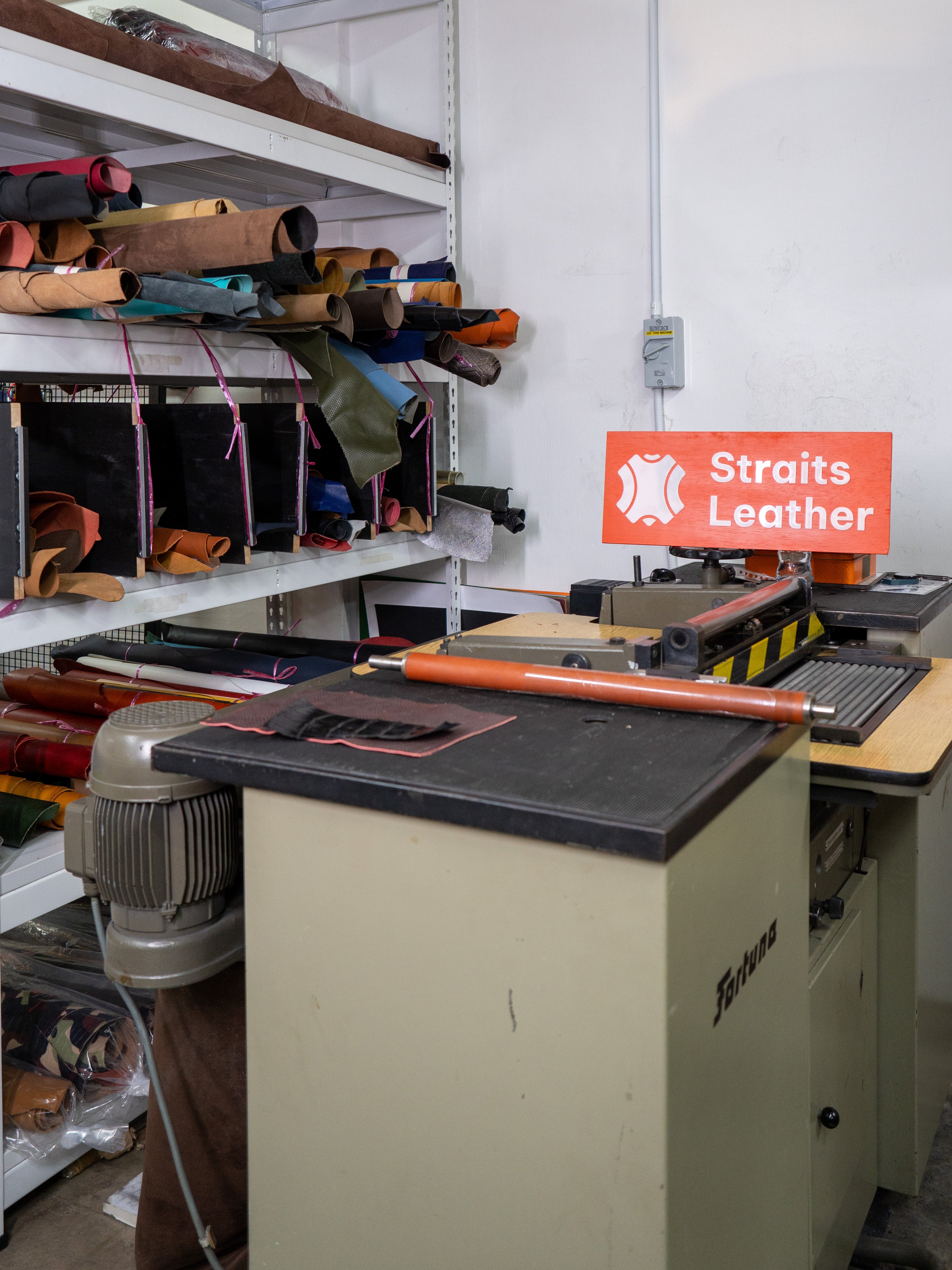 Workshop with leather products and machinery, featuring a 'Straits Leather' sign.